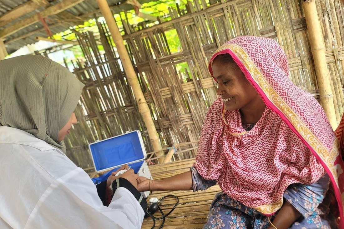 A health worker checking a woman's blood pressure during a home visit