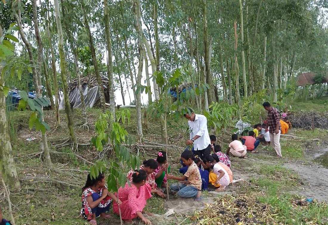 Children planting saplings along a path with an OfP staff member helping