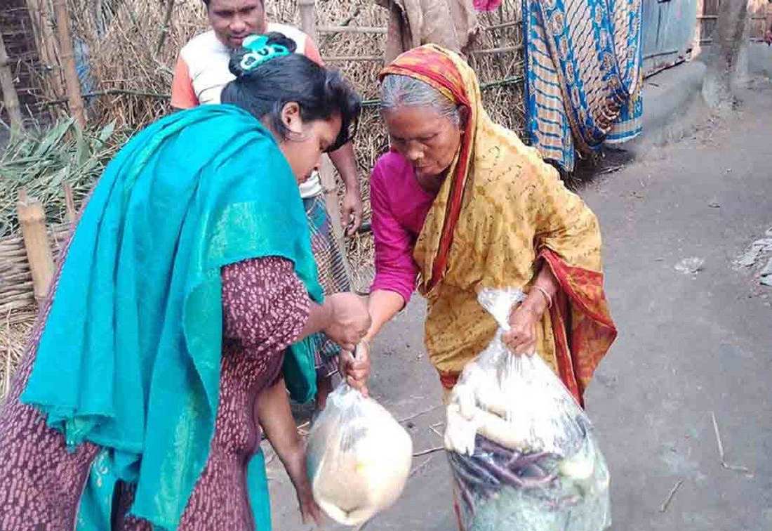 An OfP volunteer handing relief food parcels to an elderly woman in a village